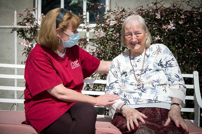 carer sitting on bench outside with senior