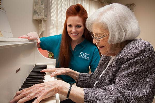 Female Right at Home caregiver watching a senior female play a piano