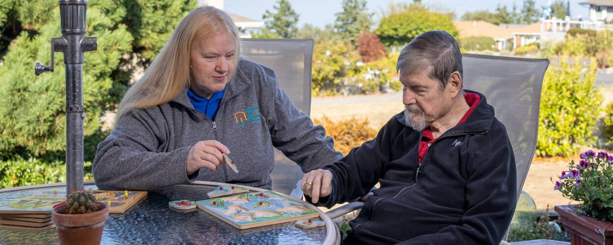 female carer playing a game with a senior male outside at a table