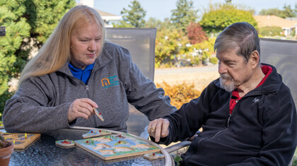 female carer playing a game with a senior male outside at a table