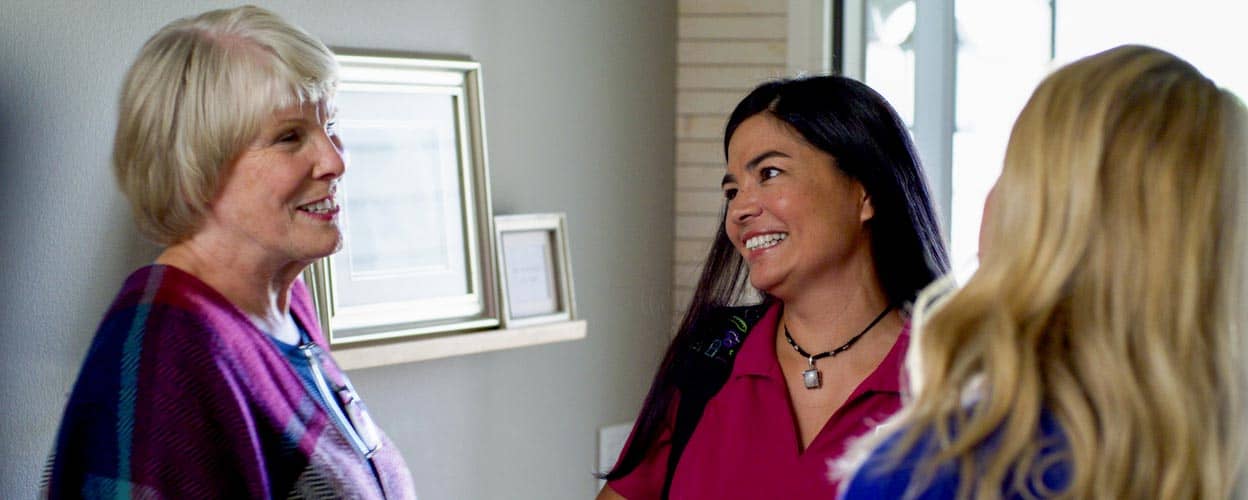 Female Right at Home Caregiver meeting a senior female and adult daughter at doorway