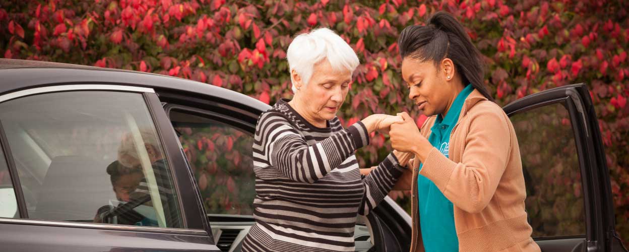 A female carer helps a senior female out of a car