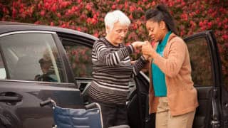 A female carer helps a senior female out of a car